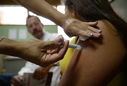 Profissional de saúde aplicando dose de vacina com seringa no braço de paciente