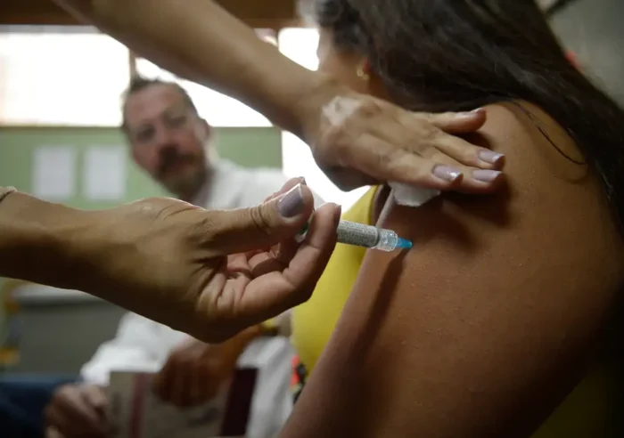 Profissional de saúde aplicando dose de vacina com seringa no braço de paciente