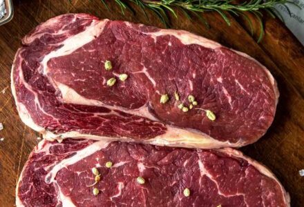 Visão superior de cortes de carne suína temperados sobre tábua de madeira.