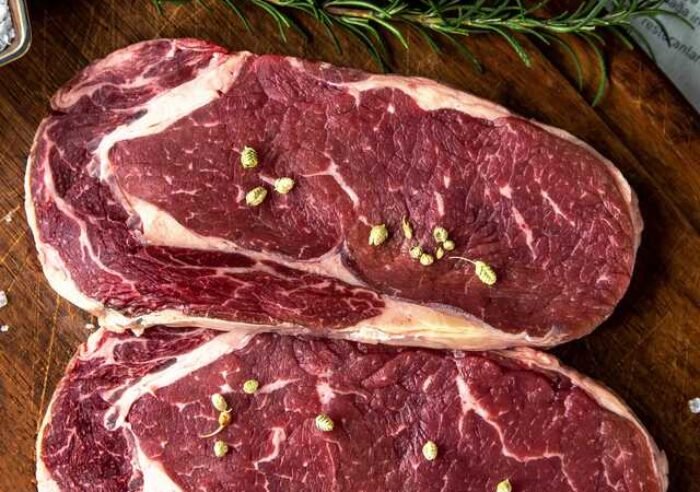 Visão superior de cortes de carne suína temperados sobre tábua de madeira.