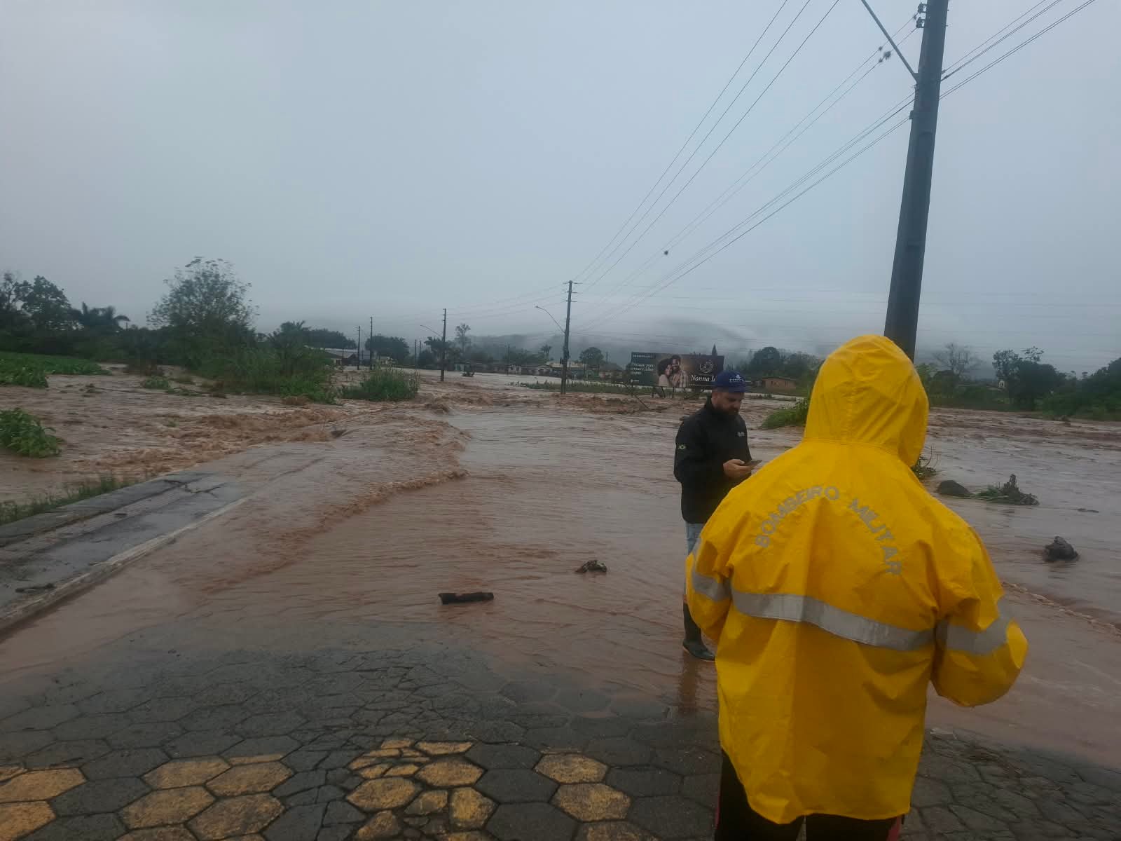 Rua alagada com água barrenta cobrindo a via e atingindo imóveis