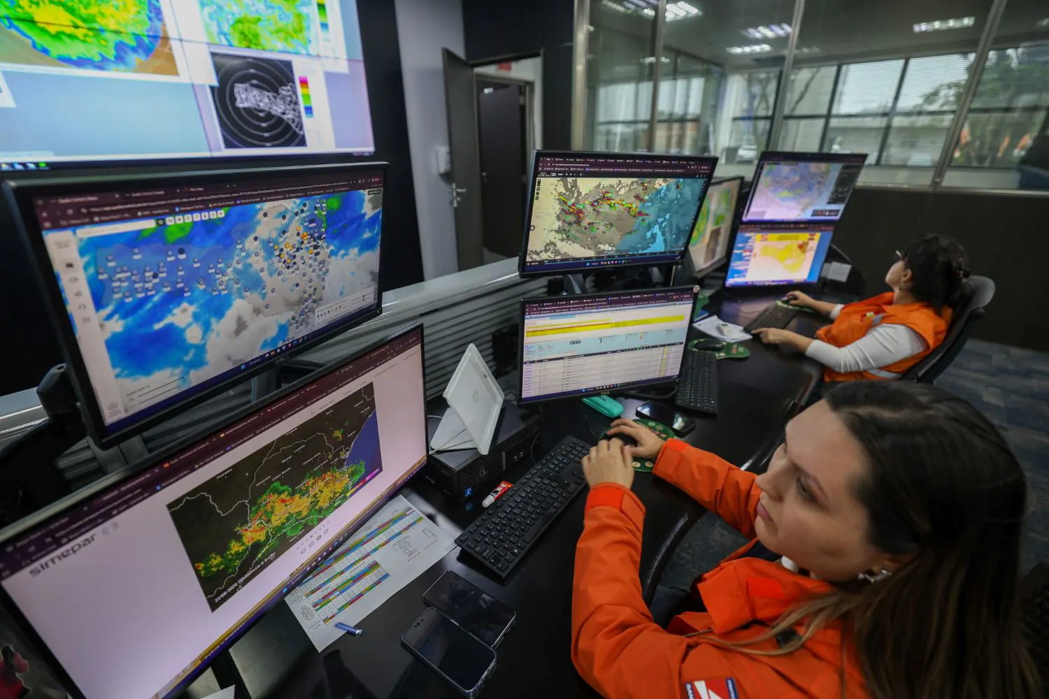 Técnico da Defesa Civil realizando monitoramento climático diante de telas de computador